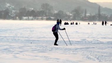 Sırtında sırt çantası olan bir kadın soğuk bir kış akşamında şehirde kayak yapıyor. Kışın aktif eğlence, kış sporları, Noel arifesinde Krakow 'da büyük karlı tarlalar.