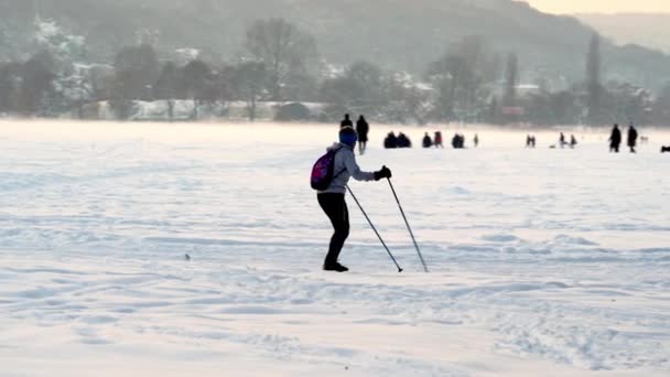バックパックを背負った女性が寒い冬の夜に街でスキーをしている 冬のアクティブなレクリエーション 冬のスポーツ クリスマスイブのクラクフの大きな雪原 — ストック動画