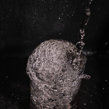 Drops of transparent water seethe in a glass, a stream of clean water, beautiful streams and splashes of drinking clean water in a transparent glass. Environmental problems, value of water resources