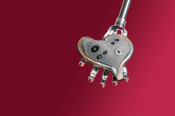 Mechanical heart in the iron hand of a robot for Valentine\'s Day. Futuristic love concept of robots and people. Heart with iron screws in the palm of a robot against a viva magenta background