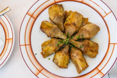 Hearts of delicious artichokes on a plate in olive oil. A minimalist view from above of artichokes on a table at an Italian restaurant. Unopened flower buds in a vegetarian kitchen Venice. Copy space