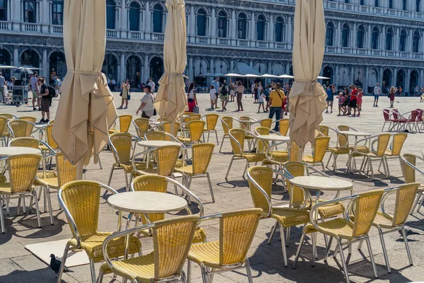 Italy, Venice, August 2022. Gold chairs in an open-air street restaurant and tourists in St. Mark's Square on a sunny summer day, the golden color of Venice