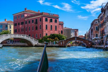 Venedik, İtalya - Ağustos 2022: Güneşli bir günde deniz sokaklarının kavşağındaki otantik renkli evler, kanallar üzerindeki taş köprüler, şehir sokaklarındaki deniz kenarındaki sokak kafelerinde dinlenen