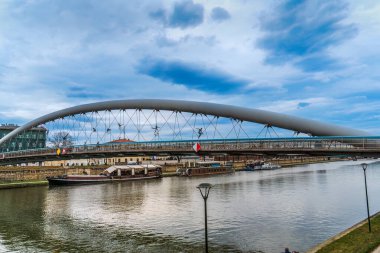 Krakow 'daki Peder Bernatek Köprüsü. Vistula ya da Wisla nehri üzerindeki Krakow Köprüsü 'nde gemiler nehir kıyısına demirlemiş, bulutlu yay gökyüzü.