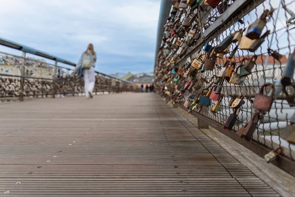 Metal locks of love on the pedestrian bridge of Father Bernatek in Krakow, a lonely girl walks on the bridge in the background, copy space, cloudy spring sky
