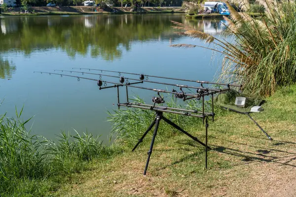 stock image Fishing rods for sport fishing on the shore of the lake on a sunny day against the background of water and reflections of the shore, a hobby for relaxation, a sustainable unity of people and nature