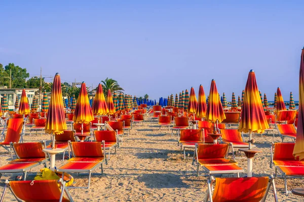 하늘을 배경으로 모래가 해변에 의자와 우산이 줄지어 대칭적 진품있는 아침의 — 스톡 사진