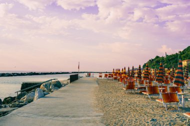 Kumsalda sabahın erken saatlerinde, güzel İtalyan plaj sahnesi, otantik panoramik manzara, güneş pansiyonları ve şemsiyeler, Adriyatik denizi, premium fotoğrafçılık, otantik plaj arka planı, bulutlu gökyüzü.