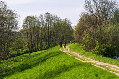 Bir grup insan baharda güneşli bir günde toprak bir yolda yürüyor, yürüyüş yolları, güzel yeşillikler, parkta ve halka açık yerlerde yürüyor. Ekolojik sanat, doğa ile birlik içinde sürdürülebilir kalkınma
