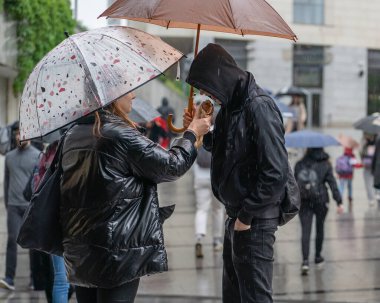 Polonya, Krakow, Mayıs 2023. Yağmurda şemsiyelerin altında randevuya çıkan bir çift, kötü hava şartlarında yoldan geçenler arasında sevgilisini turtayla besliyor.