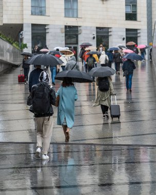 Kötü hava koşullarında yoldan geçenler şemsiyesiz ve yağmurda şemsiyesiz, yağmurlu bir yolda ıslak insanların yansımaları, yağmur damlaları ve su birikintileriyle hızlı bir şekilde yürüyorlar. Dikey mahsul