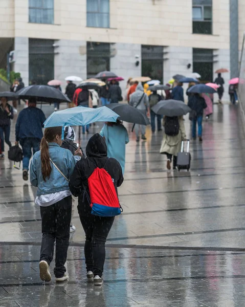 Yoldan geçenler ve turistler kötü hava koşullarında yağmurda şemsiyesiz ve şemsiyesiz hızlı bir şekilde yürürler, ıslak bir yolda ıslanmış insanların yansımaları, yağmur damlaları ve su birikintileri. Dikey mahsul