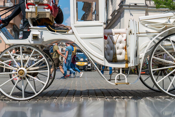 People walk on a sunny day along the cobbled street of an old European city behind a white horse-drawn carriage in the foreground, sustainable development European cities, eco-conscious consumerism
