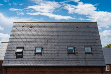 Simetrik tavan pencereleri ve büyüleyici mavi gökyüzünün altında eğimli bir çatısı olan bir İngiliz evi.