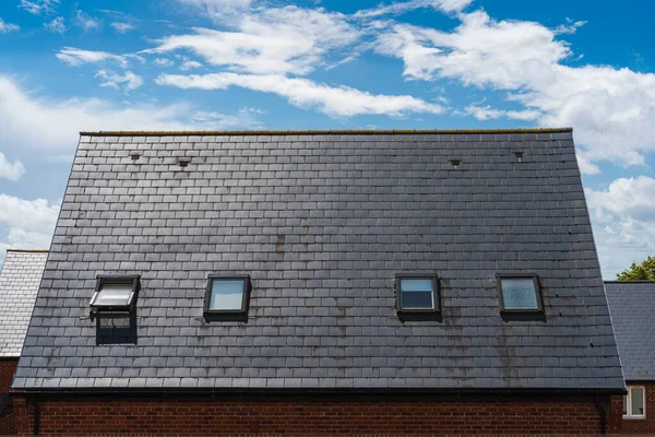 Simetrik tavan pencereleri ve büyüleyici mavi gökyüzünün altında eğimli bir çatısı olan bir İngiliz evi.