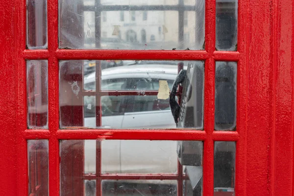 stock image Close-up of the iconic British red telephone box with pay phone inside and glass windows. Dirty glass. Urban street scene with car and building in background.