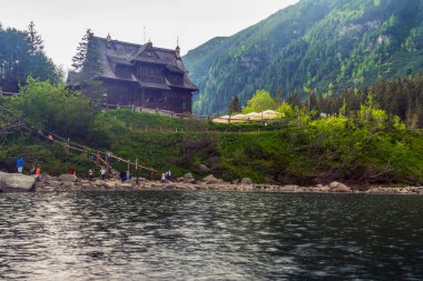 Yağmurlu bir günde Polonya Tatra Ulusal Parkı 'ndaki Morskie Oko gölünün kıyısında Chalet. Bulutlu bir günde göl, kıyıda küçük turist figürleri. Bu görüntü doğa ve seyahat için mükemmel.