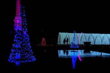 Parlak mavi bir ağaç ve parlak kemerlerle suya yansıyan canlı Noel ışıkları, tatil sezonunun neşesini ve sihrini anımsatıyor, tatil ve şenlik kavramları için ideal.