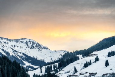 Gün batımında sakin karlı manzara, dağ sırasını ve rahat kabinleri sergiliyor, kış tatili ve doğal güzellik için ideal, seyahat, tatil ya da doğa için uygun