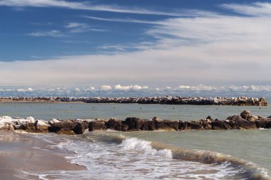 Sakin sahil manzarası, berrak sular kumlu sahili öpüyor engin gökyüzünün altında kayalık bariyerlerle çevrili.