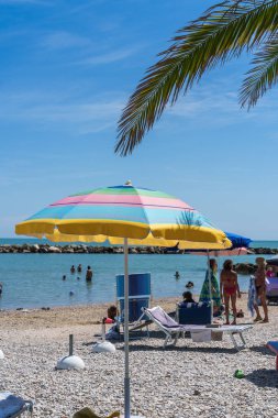 Okyanusun arka planında sakin bir plaj tatili ve mavi gökyüzü. Parlak renkli şemsiyesi, şezlongları, sakin denizi ve tatil atmosferi olan.