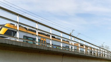 Modern elektrikli tren, açık mavi gökyüzüne karşı yükseltilmiş bir köprüde seyahat ediyor. Hareket halindeki çağdaş ulaşım ve kentsel altyapının özünü yakalar