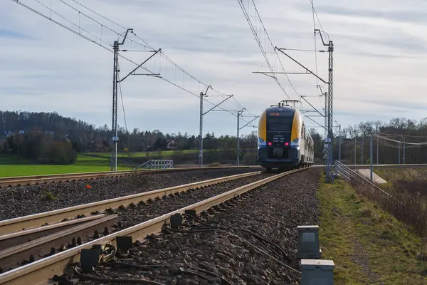 stock image yellow train on electrified railway tracks. Overhead power lines and white safety barriers visible. Railroad infrastructure showcasing public transportation and sustainable travel technology