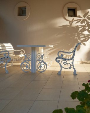 Elegant white outdoor furniture for relaxing in a quiet garden; soft sunlight casts calm shadows on the golden wall and tiled floor. Copy Space clipart