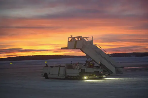 Laponya 'daki bir kutup gecesinde, canlı bir alacakaranlıkta, pistte seyyar biniş merdivenleri. Sakin havaalanı operasyonlarını ve Kuzey Kutbu hava yolculuğunun çarpıcı güzelliğini gözler önüne sermek için mükemmel.