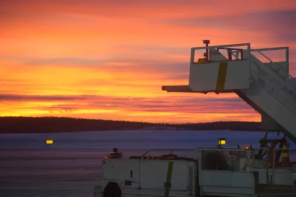 Laponya 'da bir kutup gecesinde canlı bir alacakaranlık, hareketli yatılı merdivenler günbatımının sıcak renkleriyle aydınlatılıyor. Sakin havaalanı operasyonları ve Kuzey Kutbu hava yolculuğunun güzelliği