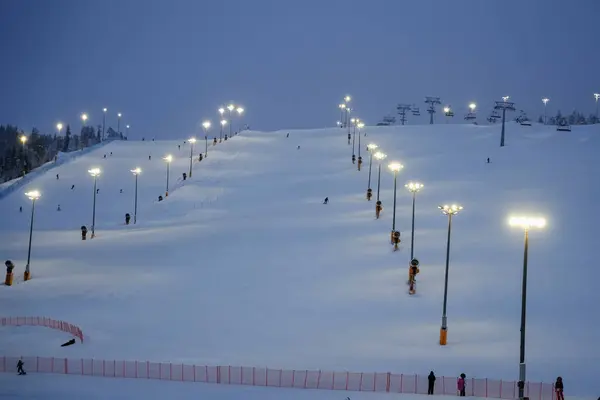 Levi Kayak Tatil Köyü, Laponya 'da büyülü kutup gecesinde kayak pisti aydınlandı. Kayakçılar yumuşak ışıklar altında sakin, karlı bir arazide inerler..