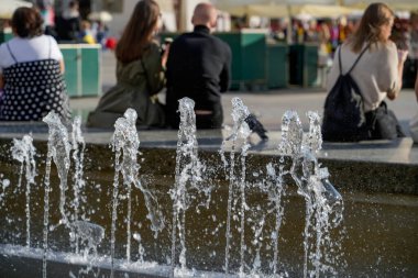 Canlı bir fıskiyenin canlı bir su püskürten manzarası. Rahat insanlar canlı bir şehir meydanındaki havanın tadını çıkarıyorlar..