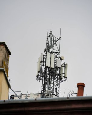 Çatıya çoklu sektör antenleri yerleştirilmiş telekomünikasyon kulesi, modern mobil ağ bağlantısı için temel altyapı, bulutlu gökyüzüne karşı kablosuz veri iletimi