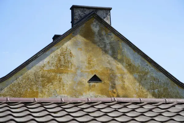 Lekeli sıva dokusu ve üçgen tavan arası menfezini gösteren yıpranmış eski bir binanın detaylarını kapat. Çürüme, çatı kiremitleri ve baca kaplamalı mimari fotoğraf.