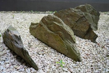 Zen ya da Japon tarzı bir kaya bahçesinde, hafif çakıllardan oluşan bir yatakta dizilmiş, huzur ve doğal huzuru çağrıştıran desenli açısal kayaları kapatın..