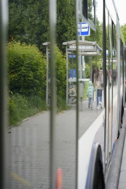 Bir toplu taşıma aracının içinde, dışarıda otobüs durağında bir ailenin görüldüğü iç korkulukların pencere yansımaları, yolcu perspektifi