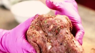 A chef's hand rubs a raw piece of meat with spices