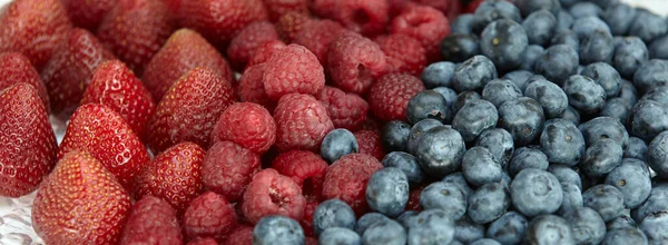 Multicolored background of natural berries: raspberries, blueberries, strawberries. Dark blue and red background color. Close-up of berries