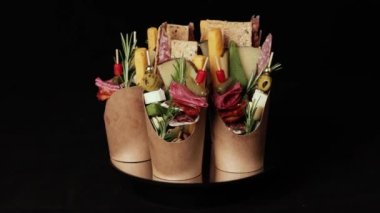 Peynirli, salamlı, zeytinli ve fındıklı Charcuterie bardakları. Aperatifler, atıştırmalıklar. Şarküteri konileri siyah arkaplan üzerinde döner