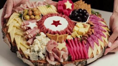 Şef, et ve peynirle birlikte meze tahtasını tanıtıyor. Çeşit çeşit peynirli aperatif tahtaları, salam, jambon, zeytin ve fındık. Şefin ellerine yakın çekim.