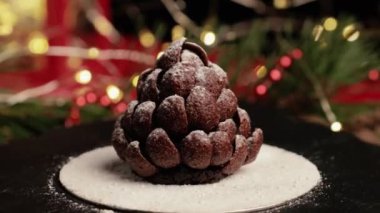 Kara tahta üzerinde dönen ladin ya da çam kozalağı şeklinde el yapımı çikolatalı tatlı pasta. Şef tatlıya pudra şekeri serper. Noel ve yeni yıl arifesi için tatil pastası.