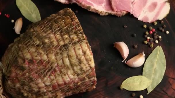 一块大的猪肉火腿和切碎的火腿在木筏木板上旋转 烤肉和调味品的特写 循环视频 顶部视图 — 图库视频影像