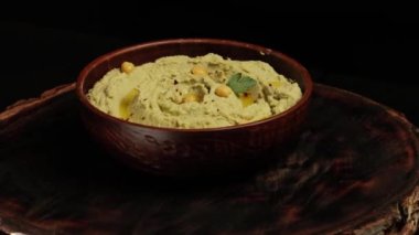 Tahta bir tahtanın üzerinde kahverengi bir seramik kasede humus. Vejetaryen yemeği. Döngülü video