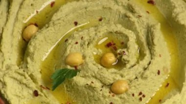 Tahta bir tahtanın üzerinde kıvrılmış kahverengi bir seramik kasede humus. Vejetaryen yemeği. Kamerayı genel bakış açısından yakınlaştırıyorum.