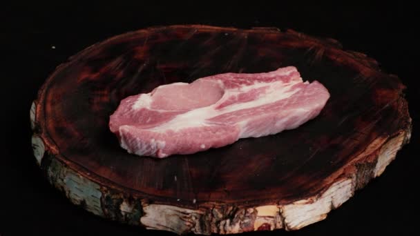 シェフの塩とスパイスは クラフトの木製板に揚げる ポークステーキ ための生の新鮮な豚肉の一部です ブラックバックで閉じる フロントビュー — ストック動画