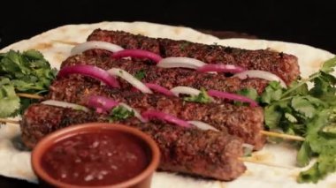 Kebap: ızgara sosis, kıymalı et şişi, pita ekmeği ve barbekü sosuyla süslenmiş, soğan turşusuyla yavaşça ahşap bir tahtanın üzerinde döndürülmüş. Doğu mutfağı. Döngüye alınmış video