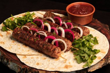 Kebap: Ahşap bir tahtanın üzerine soğan turşusuyla süslenmiş pita ekmeği ve barbekü sosuyla kıyılmış et şişleri üzerinde ızgara sosis. Doğu mutfağı.