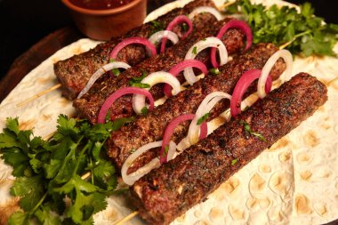 Kebap: Ahşap bir tahtanın üzerine soğan turşusuyla süslenmiş pita ekmeği ve barbekü sosuyla kıyılmış et şişleri üzerinde ızgara sosis. Doğu mutfağı.