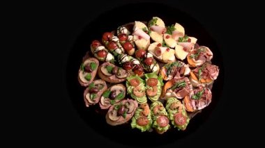 Açık büfe için çeşitli bruschetta ile aperatif tahtası: jambon, jambon, börek, domates, peynir. Aperatif tabağı siyah arka planda dönüyor. Üst görünüm, genel görünüm