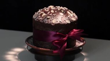 Çikolata hamurundan yapılmış Panettone (Kulich, Paska) toz şeker ve çikolata kaplama süslemeleri ile siyah beyaz arka planda kısa ışık parlamaları ile döner. Döngü videosu